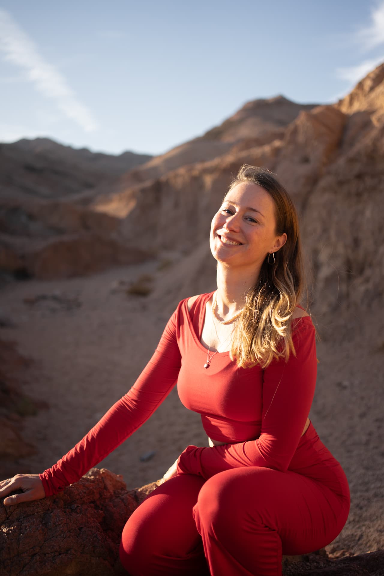 Claudia zit lachend op een rots in de woestijn in warm avondlicht